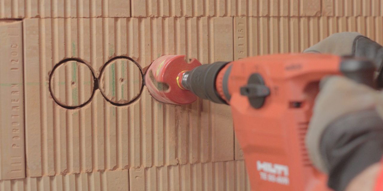 Male hands holding drill and cutting a holes for electrical boxes in a brick wall